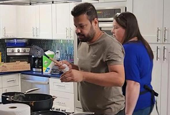 A man is standing at a kitchen counter seasoning food in a pan
