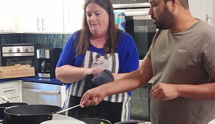 Two people cooking together in a modern kitchen, preparing food on a stovetop with various ingredients on the counter.