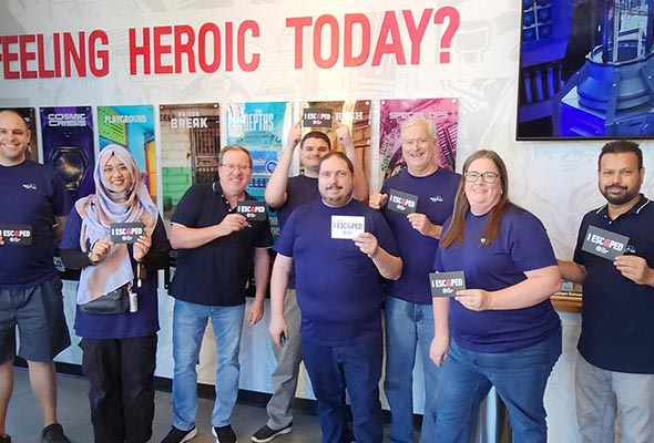 A group of coworkers standing together and holding “I Escaped” signs in front of a wall