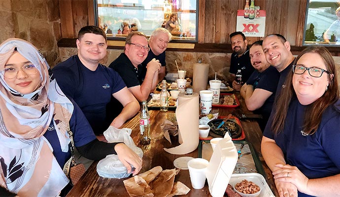 Group of colleagues enjoying a meal together at a restaurant, smiling and sitting around a wooden table.