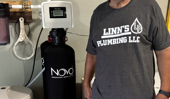 A linns plumbing professional standing next to a Novo water softener system